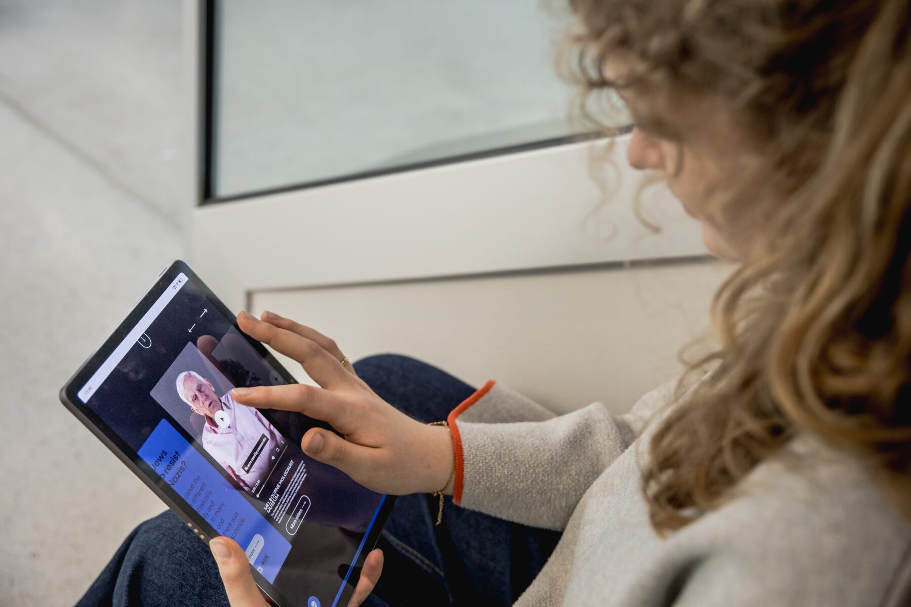 Person mit lockigem Haar bedient Tablet mit Porträtfoto und Text auf dem Bildschirm