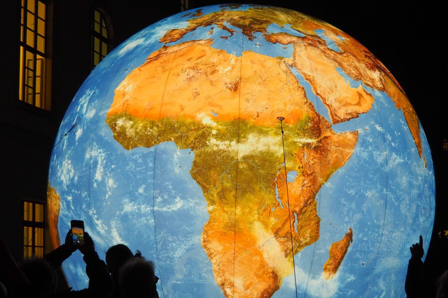 Große beleuchtete Erdkugel mit Afrika im Zentrum, umgeben von Menschen, von denen einige Fotos machen