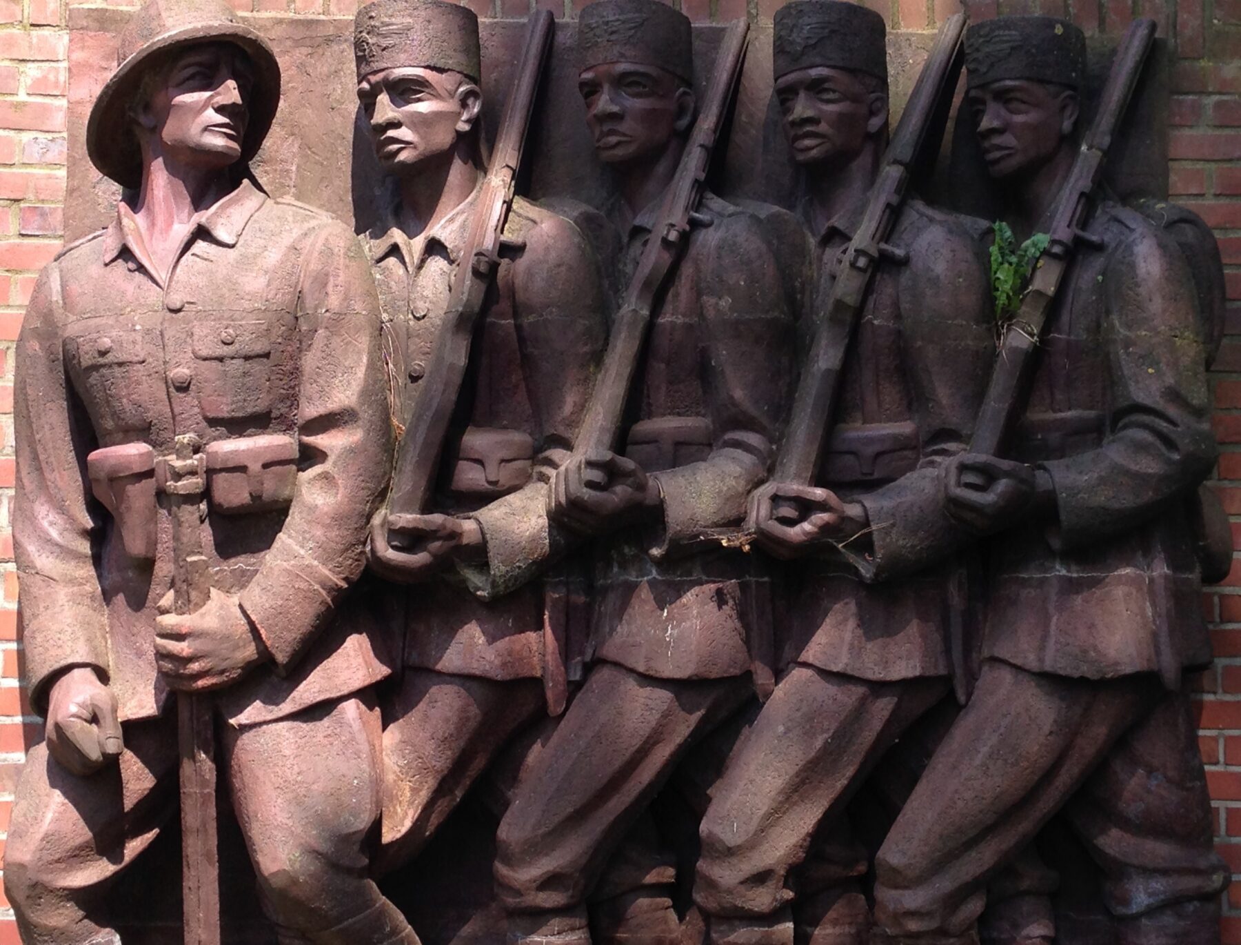 Relief mit fünf Soldaten in Uniform, vier mit Gewehren, an einer Backsteinwand