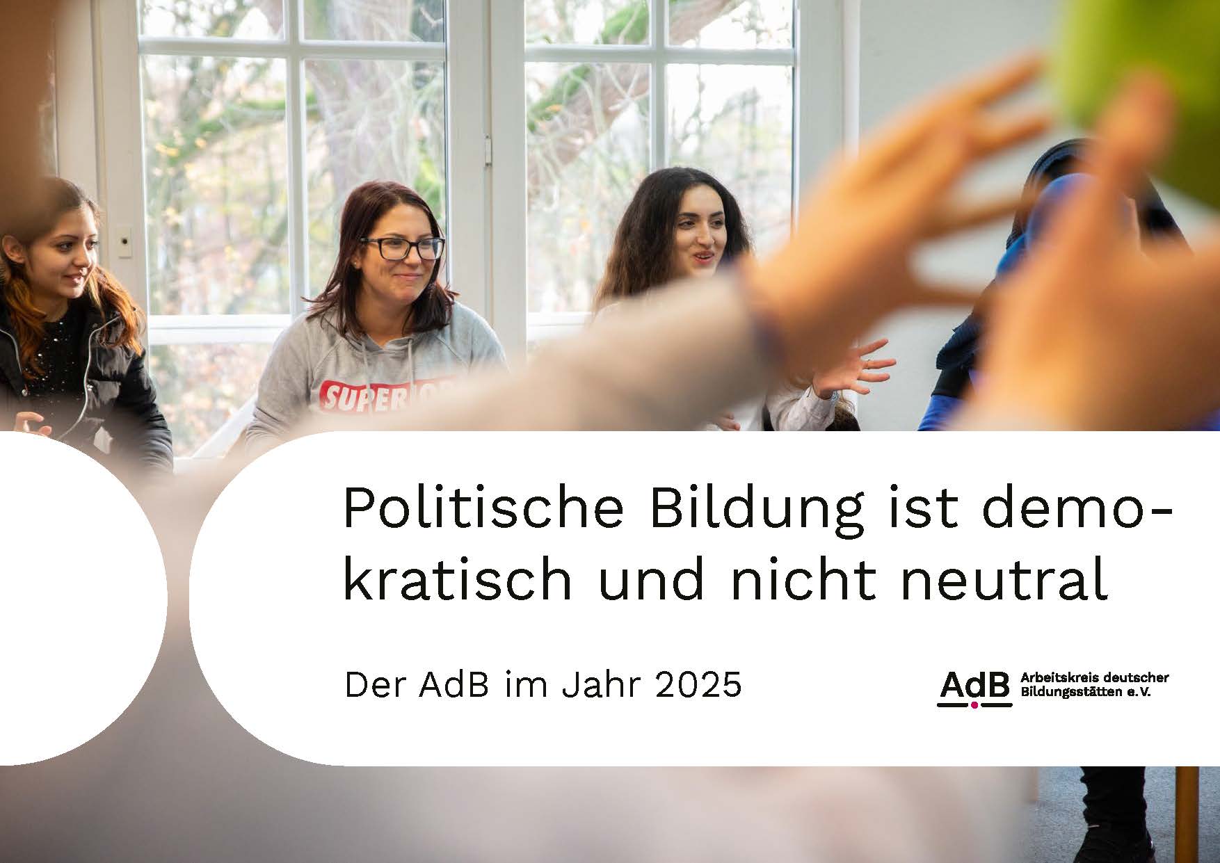 Gruppe junger Menschen sitzt in hellem Raum vor großen Fenstern. Im Vorderund fängt jemand einen grünen Ball